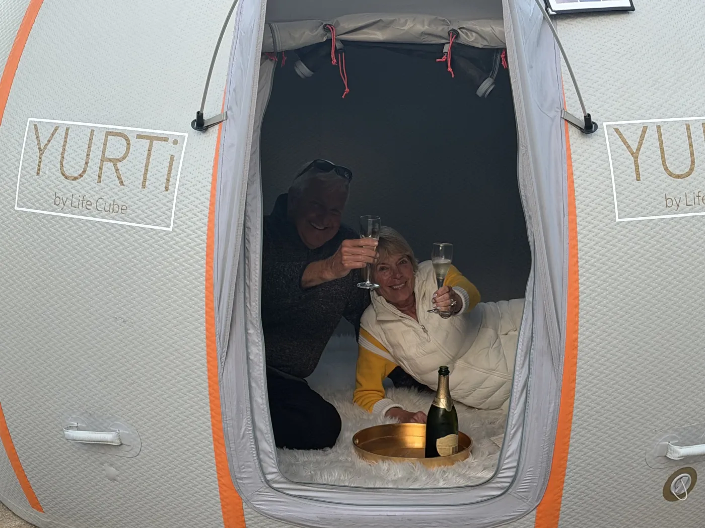 Couple toasting with champagne inside a YURTi, seen through the open doorway