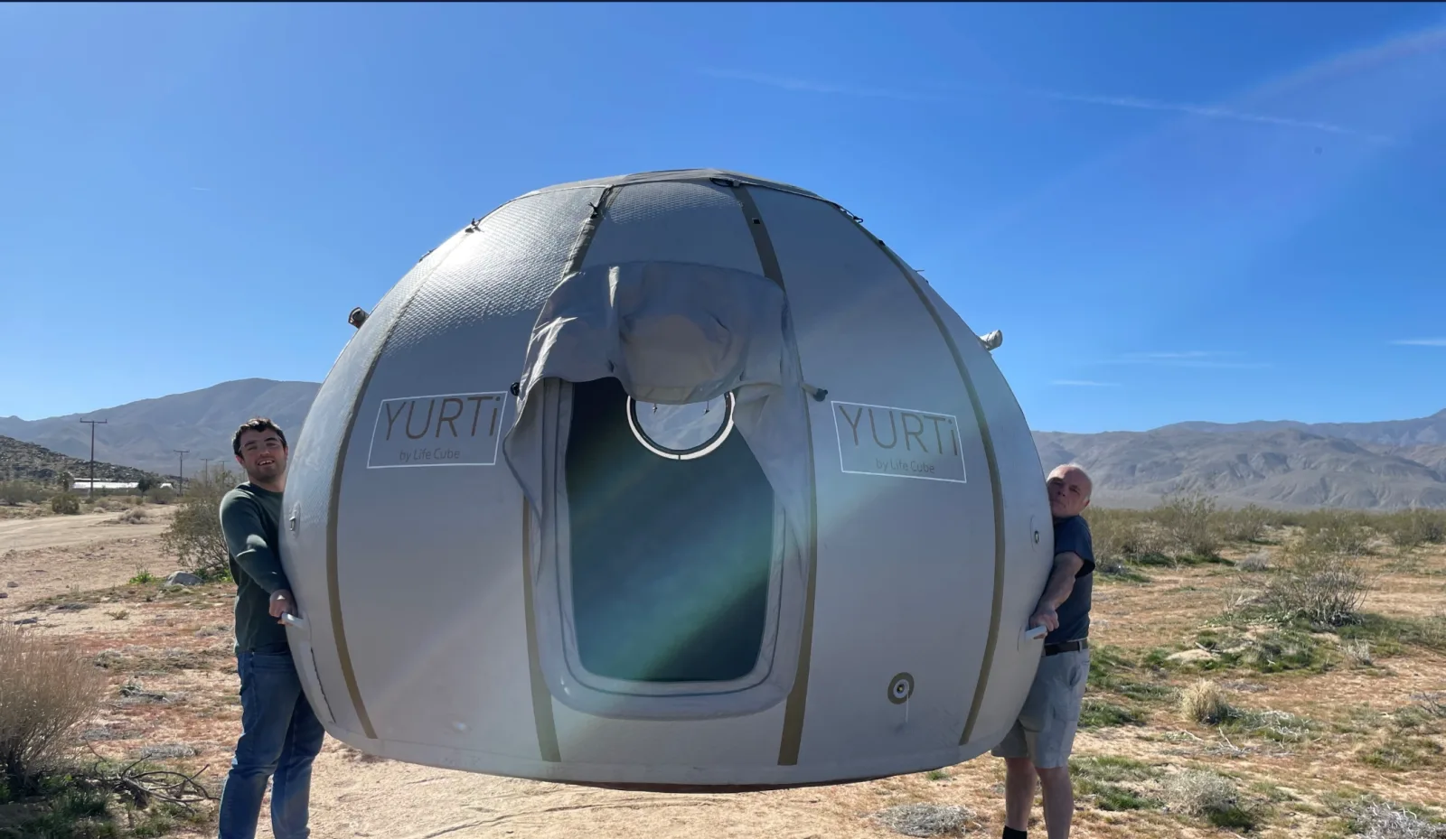 Two people lifting an inflated YURTi by hand in the desert, showing how light it is
